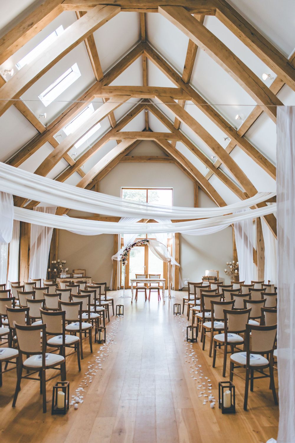 An elegant wedding ceremony venue with wooden beam ceiling, white draping, and rows of chairs down the aisle.