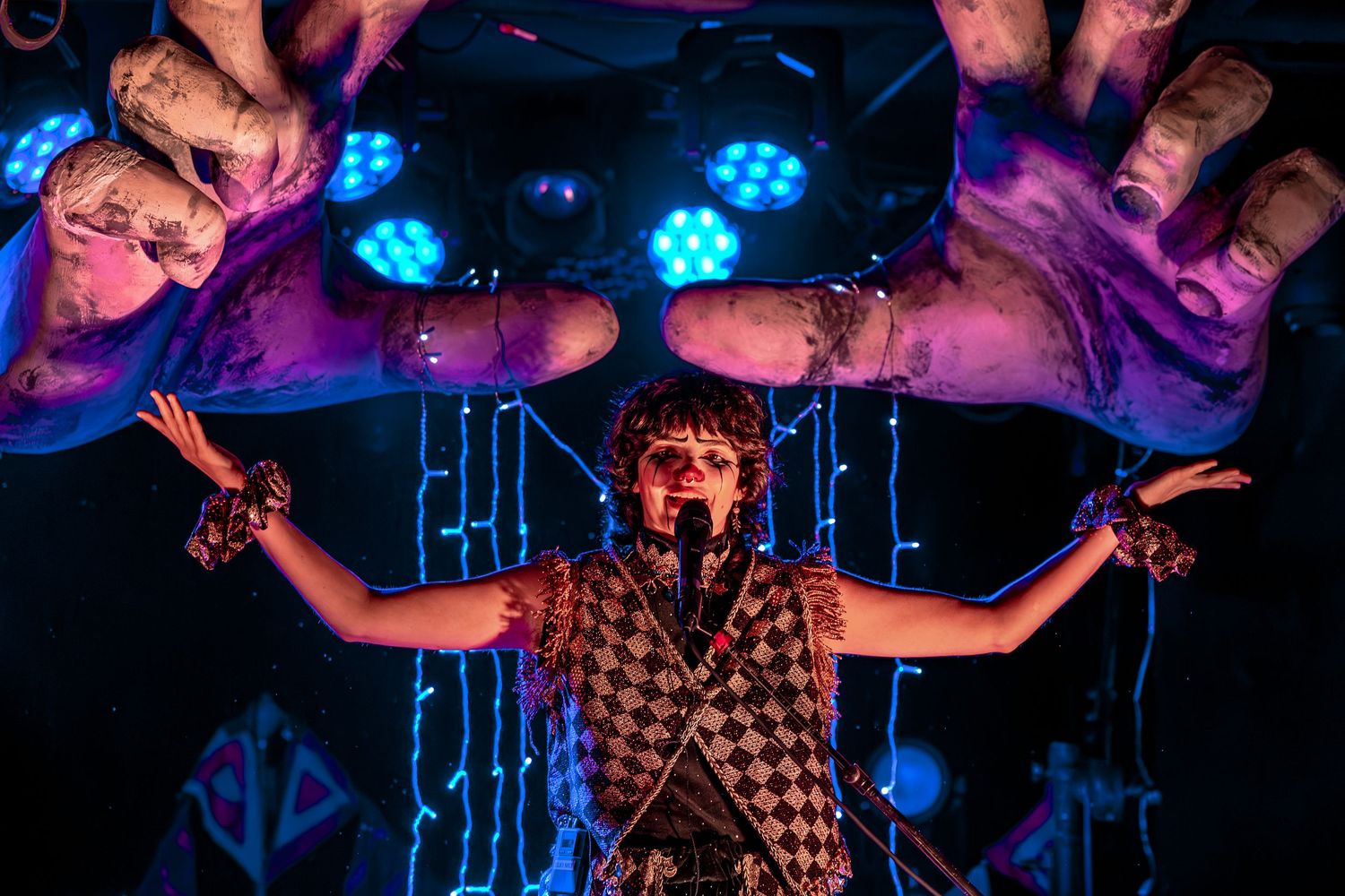 Concert performer on stage with colorful blue lighting and dramatic hand gestures during live music performance.