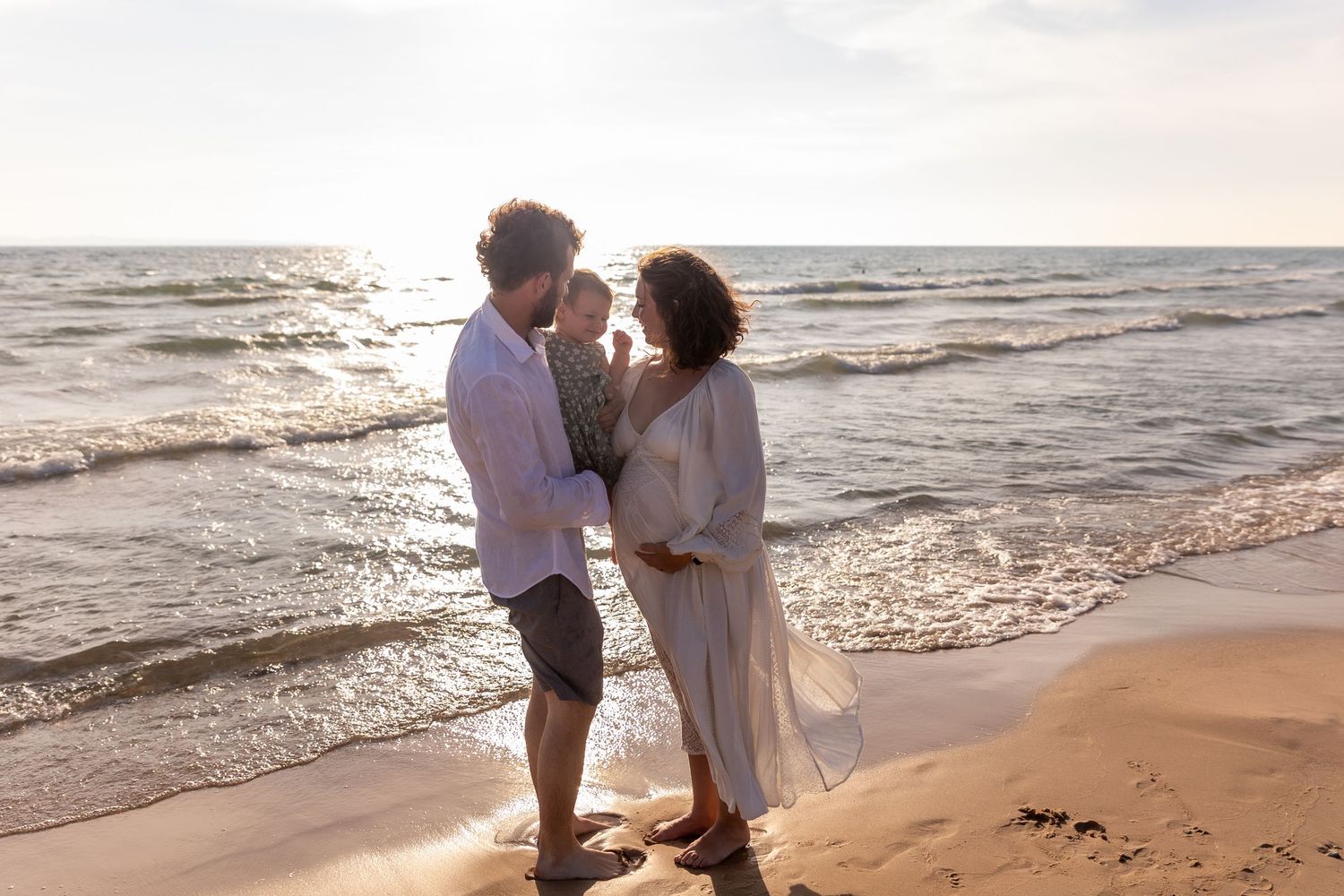 A family of three shares a tender moment on a sandy beach at golden sunset.