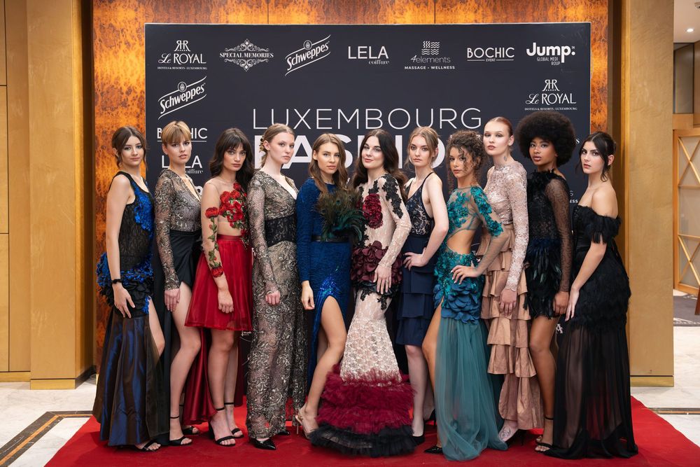 A group of elegantly dressed models pose together at the Luxembourg Fashion Week red carpet event.