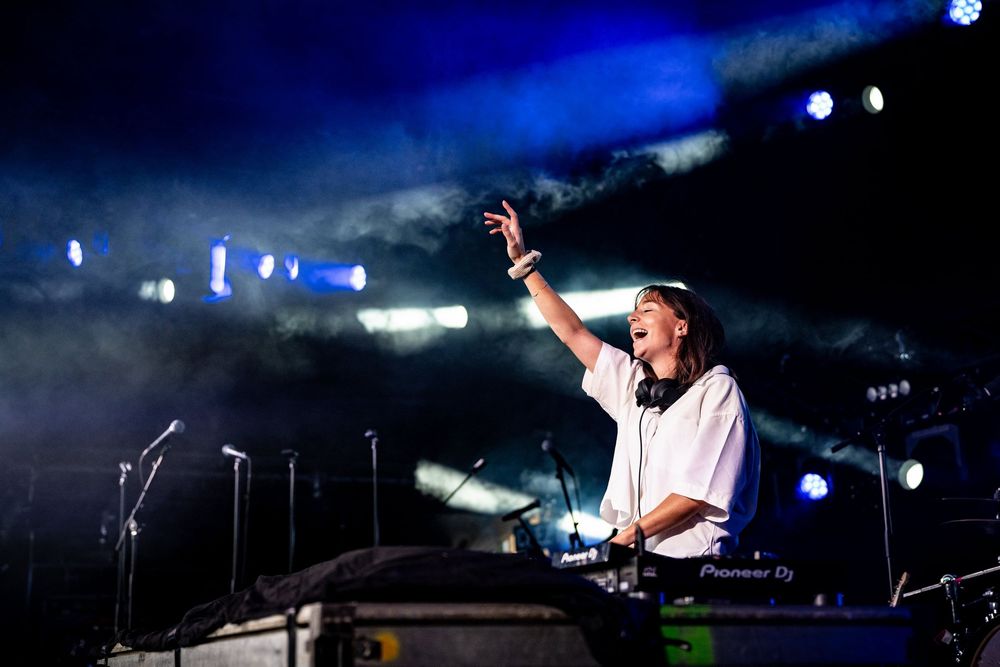 DJ performing on stage with blue lights and smoke at concert.
