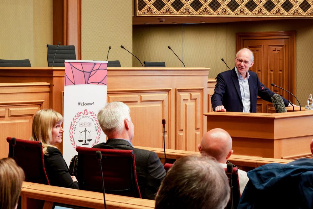 Speaker presenting at a formal legal conference podium to a seated audience in a courtroom.