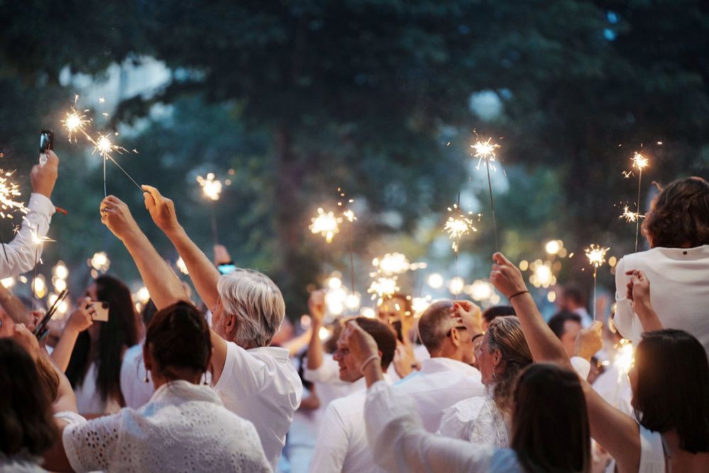 Crowd of people dressed in white holding sparklers at an outdoor evening celebration event.