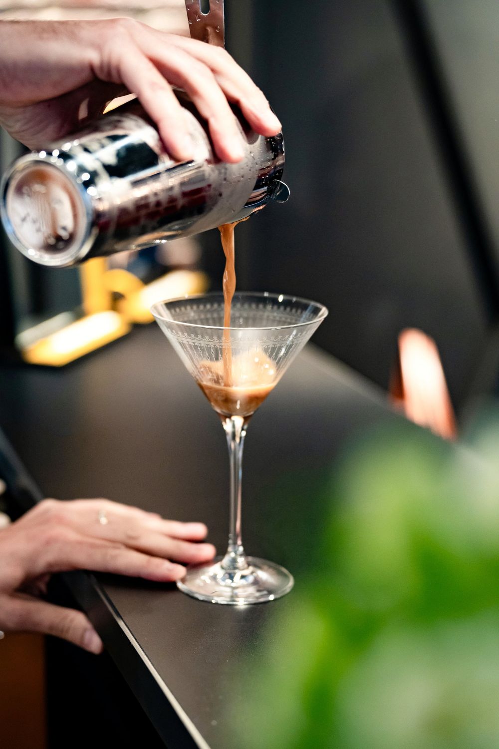 Bartender pouring an espresso martini cocktail from a shaker into a martini glass.