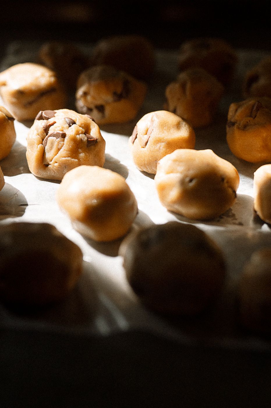 Freshly baked dinner rolls arranged on a baking sheet with dramatic lighting and shallow depth of field.