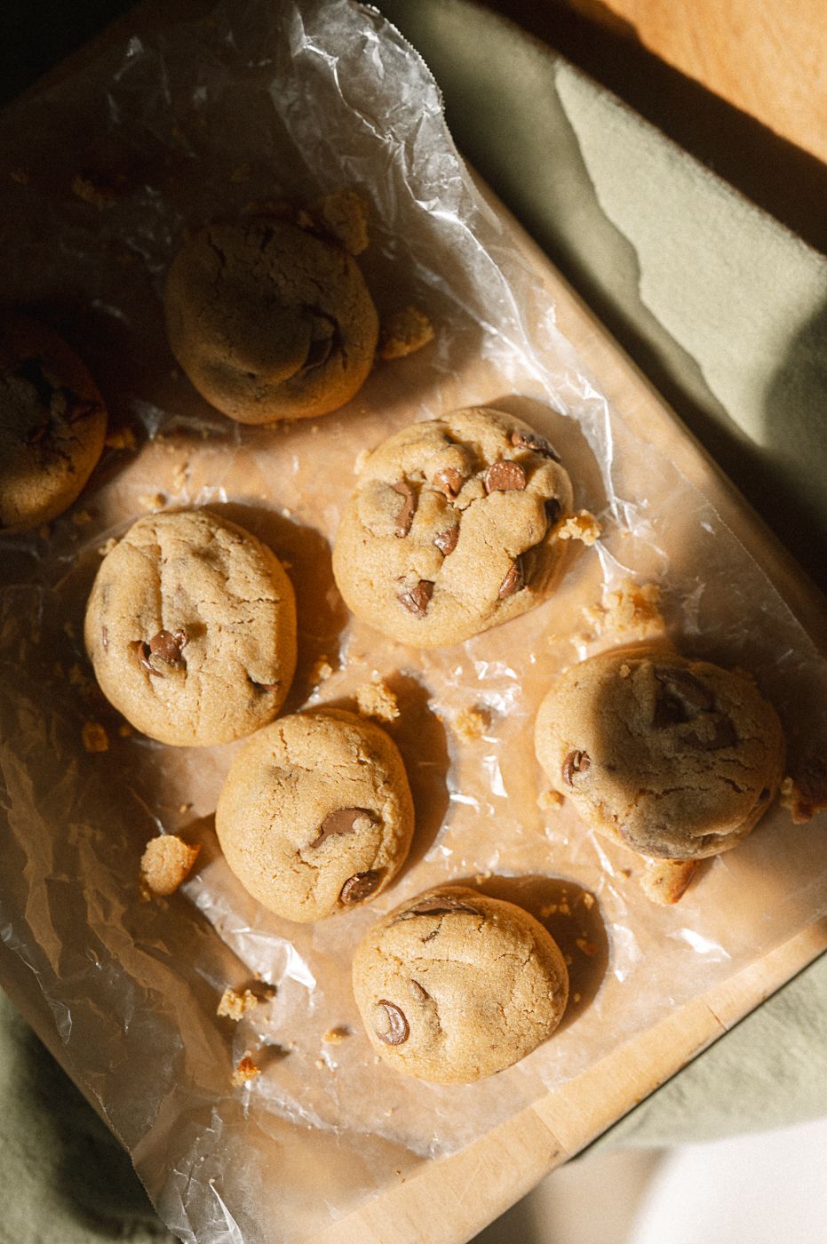 Chocolate chip cookie dough being mixed and shaped on a wooden cutting board surface.