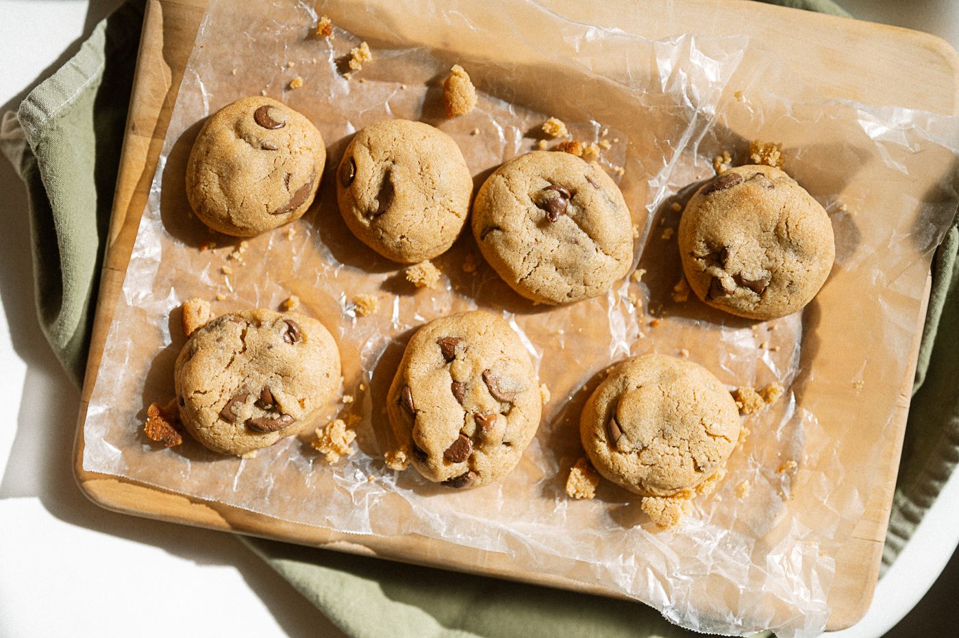 Homemade chocolate chip cookies cooling on parchment paper with golden brown edges and melted chocolate chips.