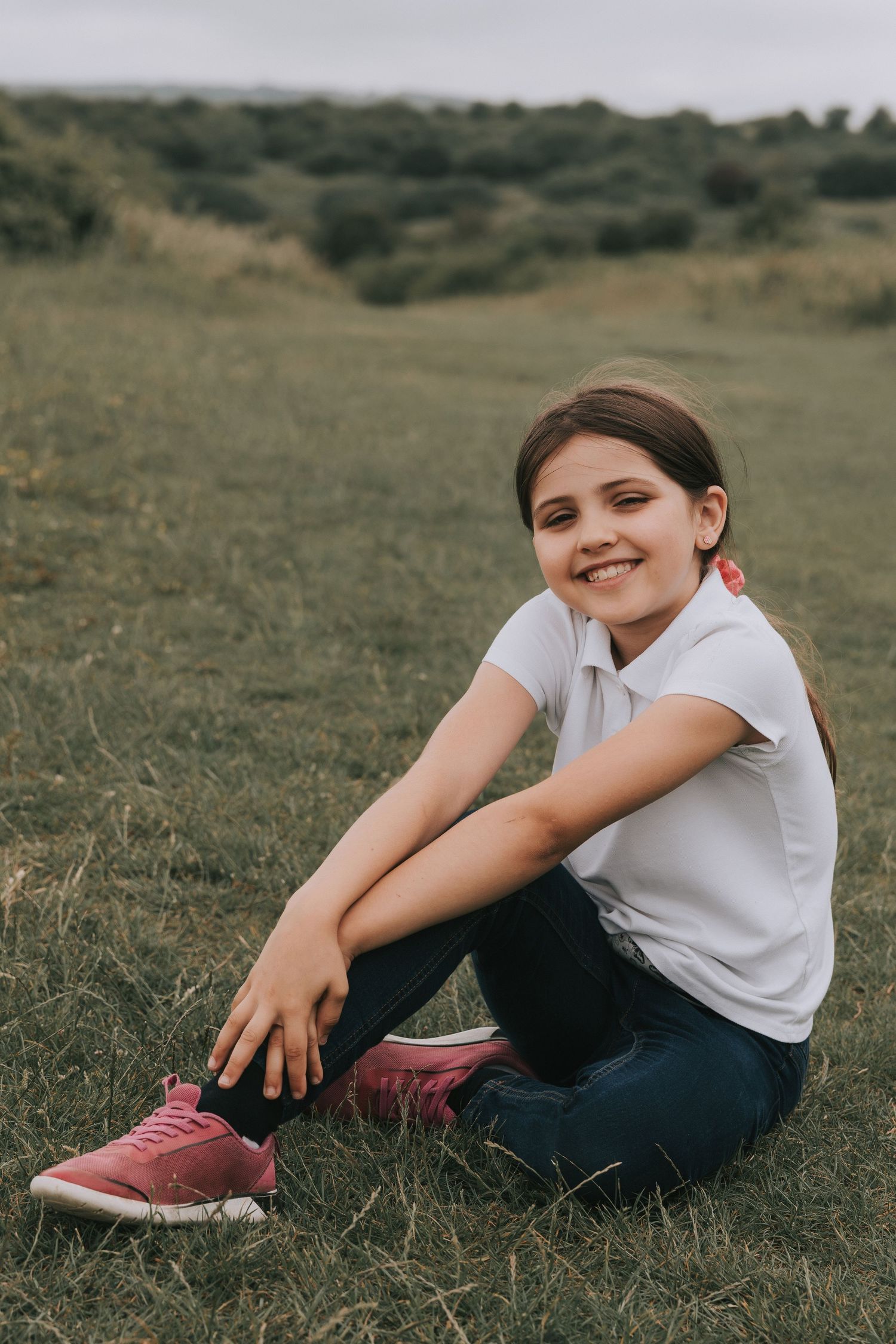 Person in white shirt and dark pants sitting casually on grassy hill.