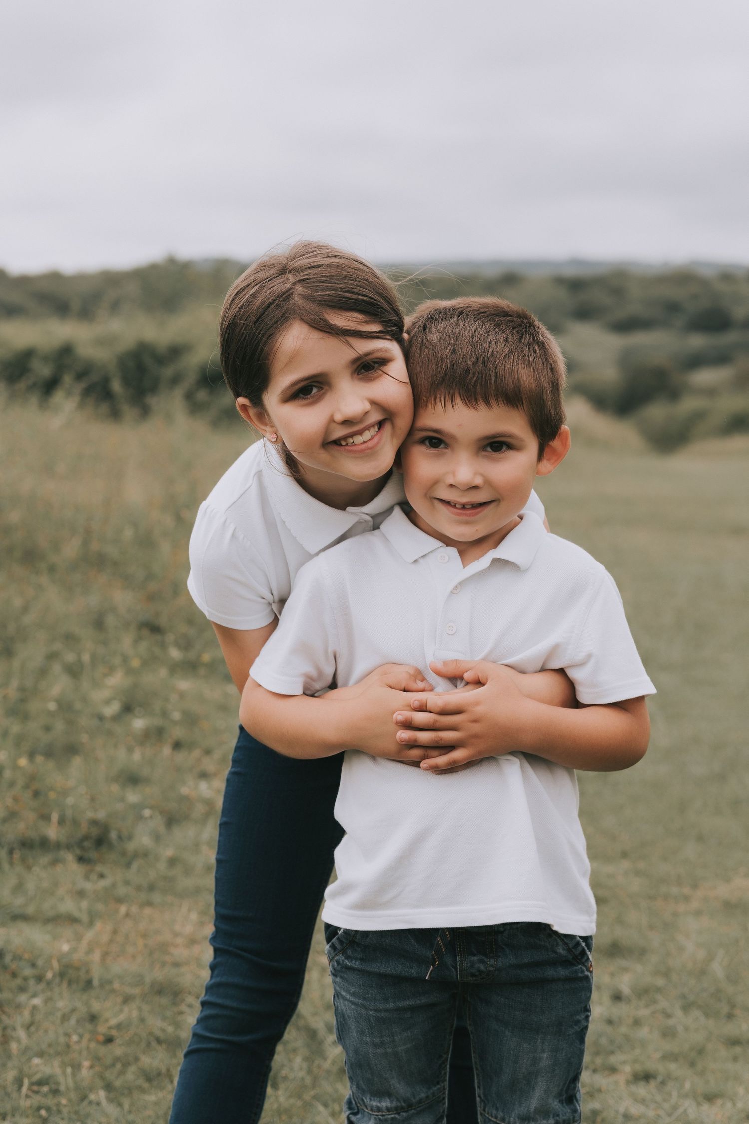 Candid outdoor portrait of two people embracing on grassy hillside.