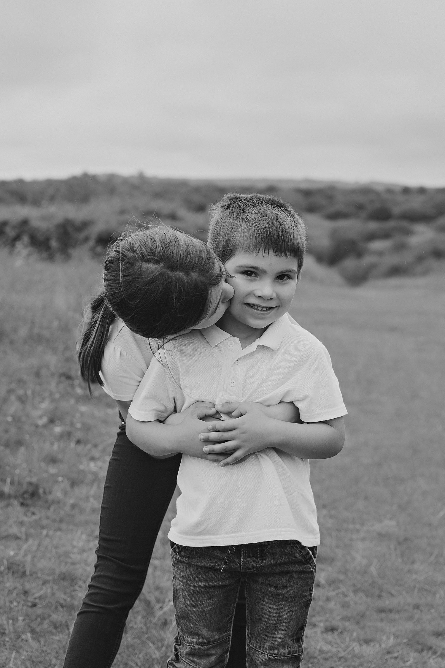 Black and white portrait of two people sharing an affectionate moment outdoors.