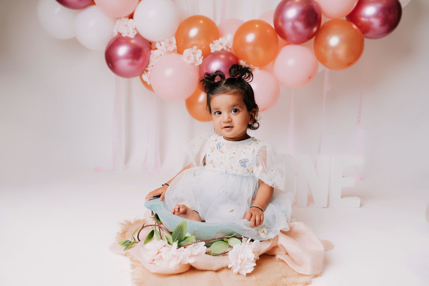 Baby's first birthday cake smash setup with pink and orange balloon decorations.