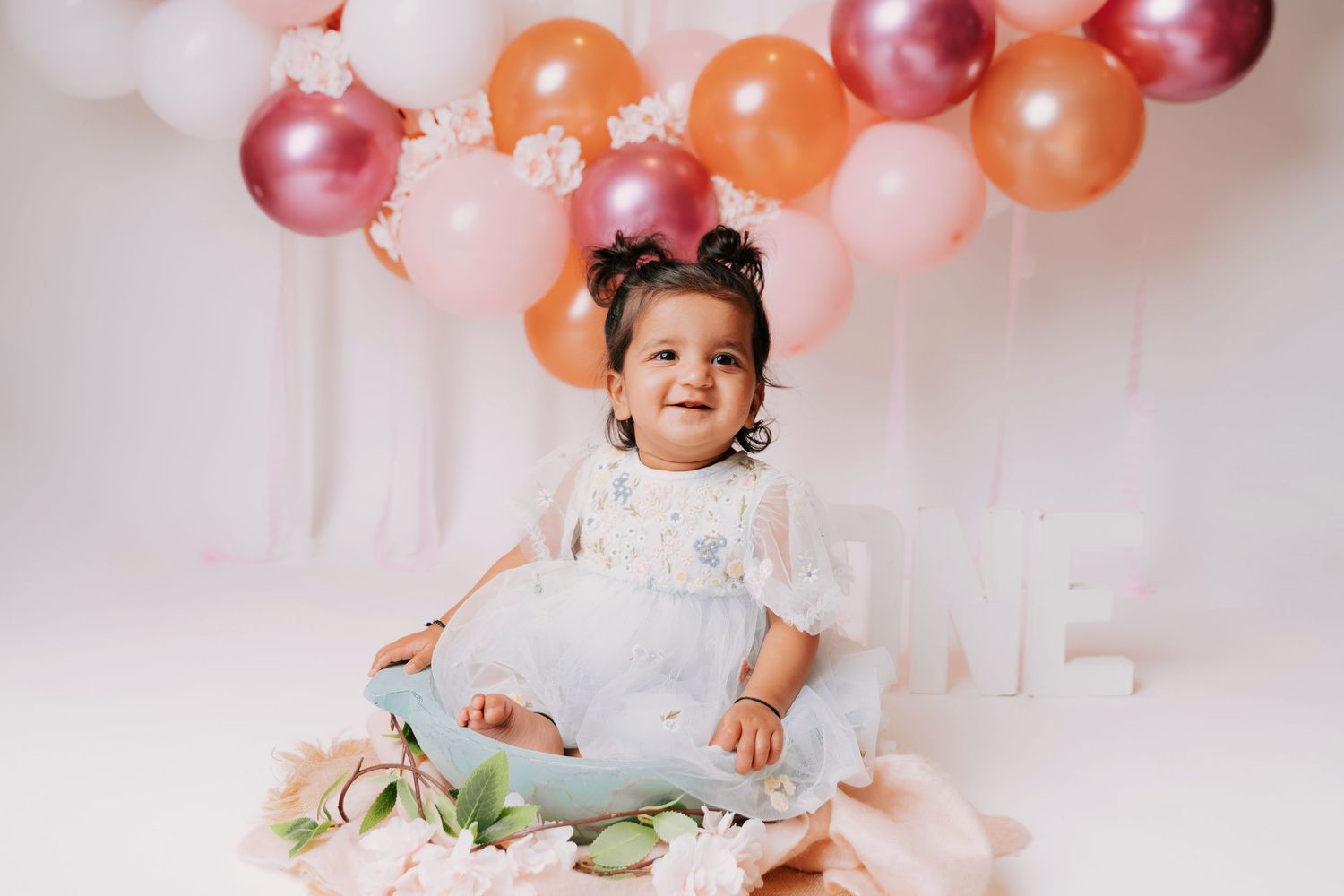 First birthday celebration photoshoot with balloon decorations in soft pink and orange.