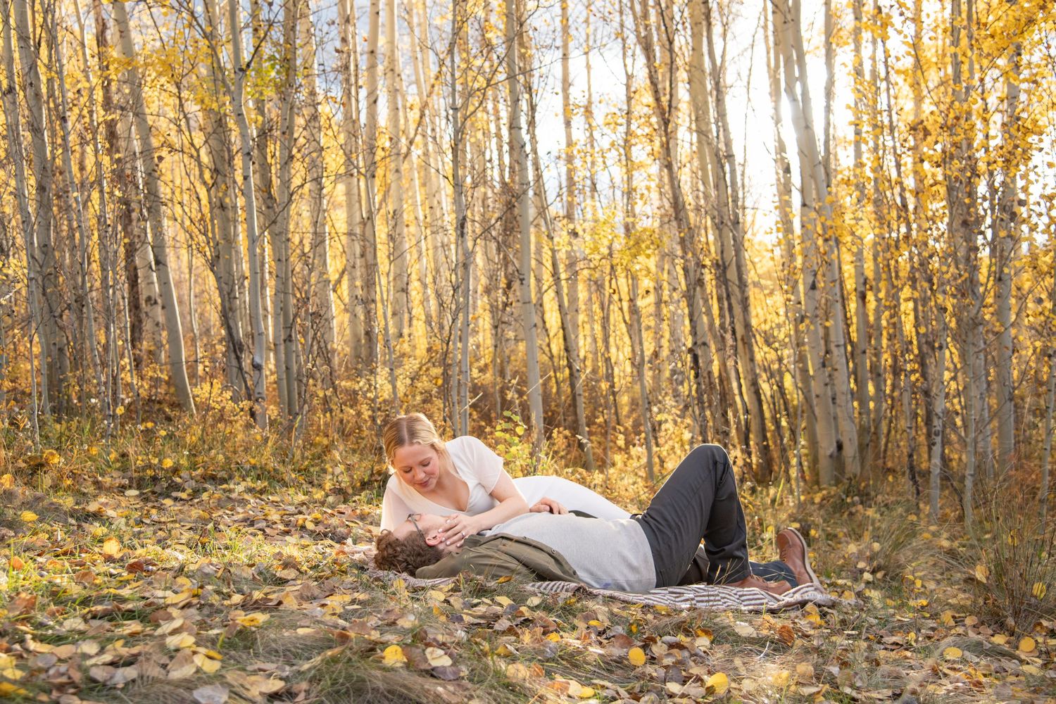 Romantic engagement session in Vail Colorado with couple laying on a forest floor covered in fall foliage and yellow aspen leaves
