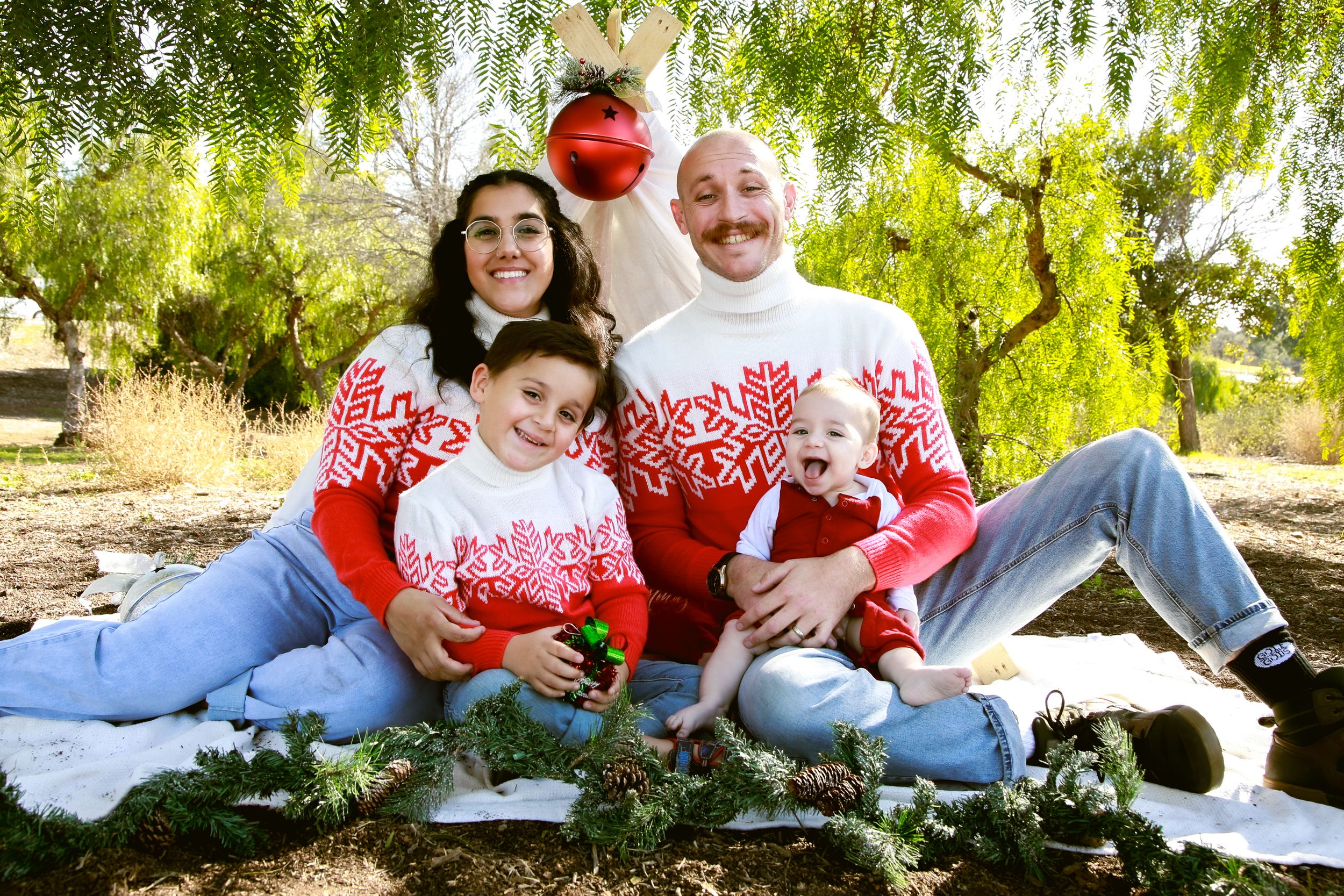 Family wearing matching red and white outfits for holiday photos under willow tree.