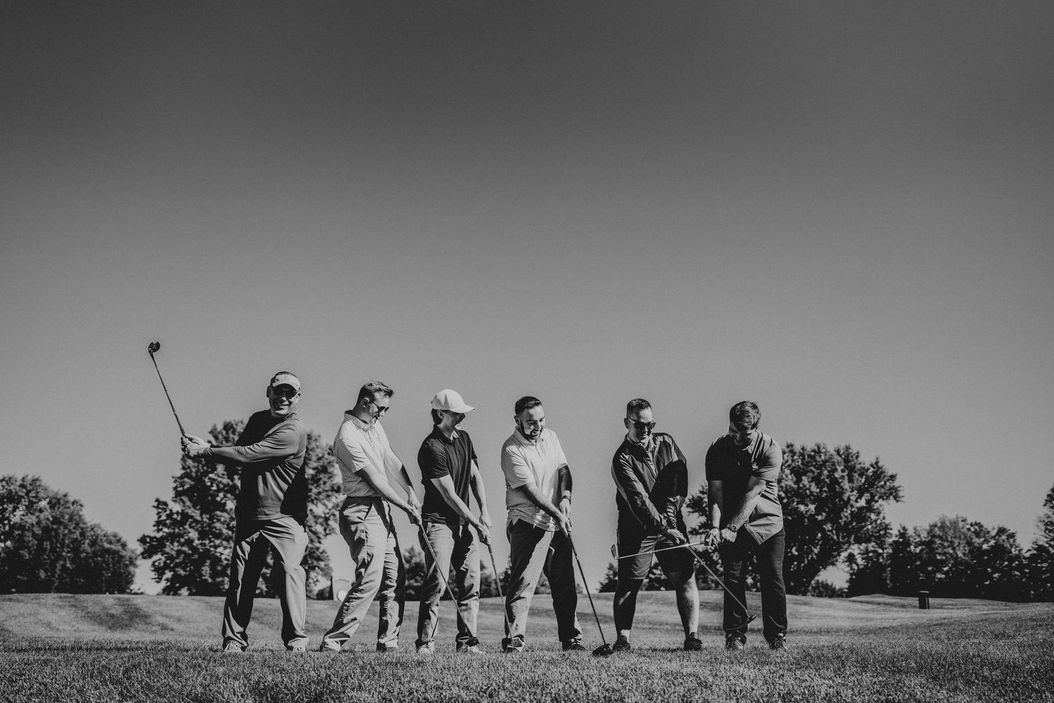 Silhouettes of wedding party members standing in a line against a bright sky outdoors.