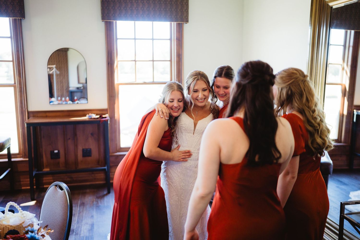 A group in red dresses gathers in an elegant room with wood paneling and windows for a formal event.