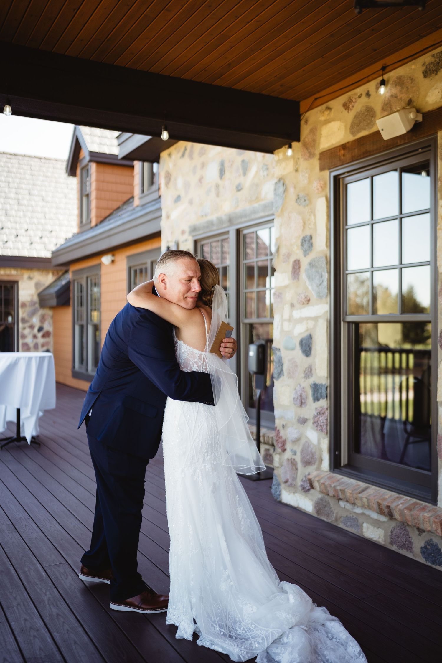 A couple embraces on a covered porch with stone walls and wooden ceiling during an intimate wedding moment.