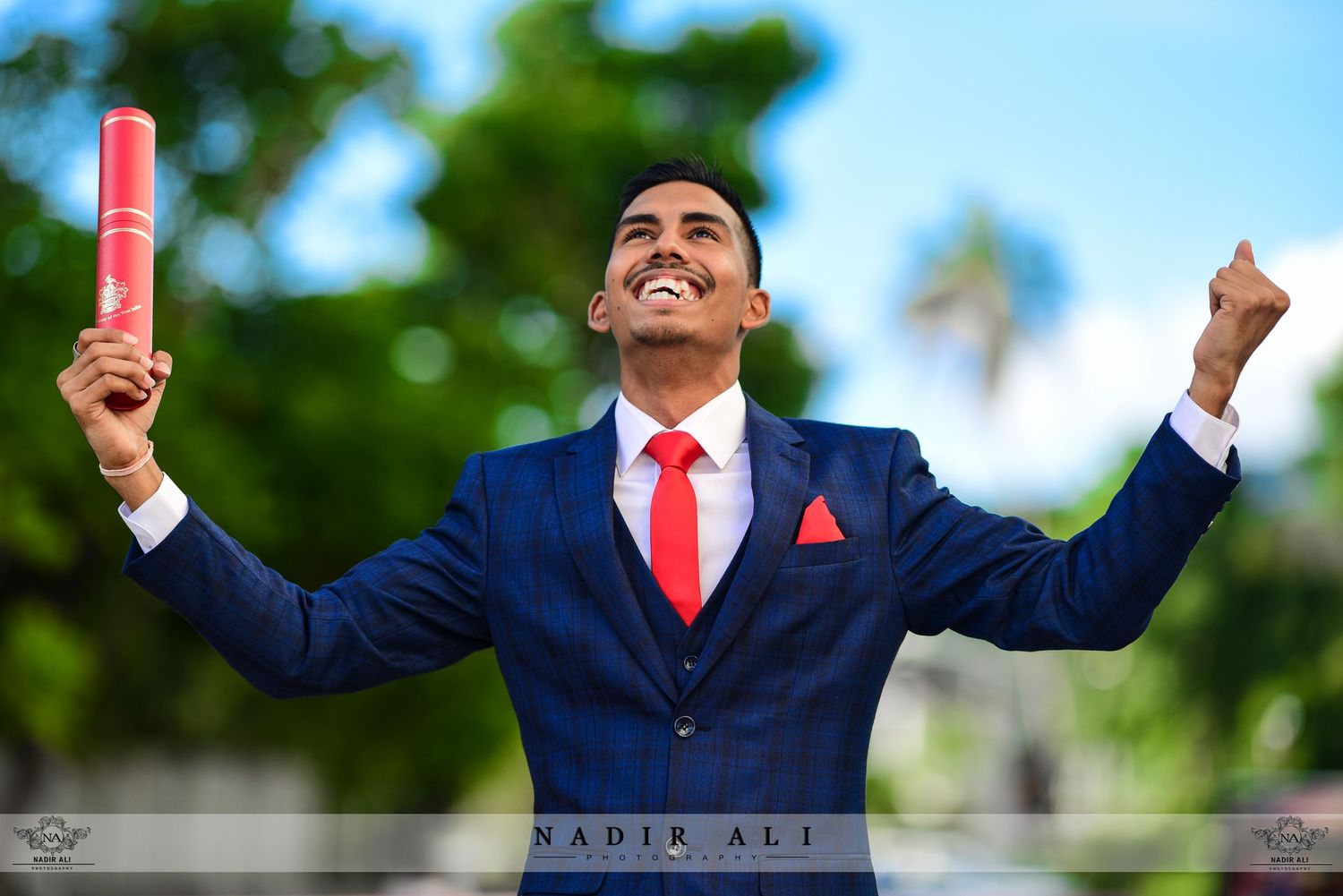 Business professional in navy suit celebrating with raised arms outdoors.