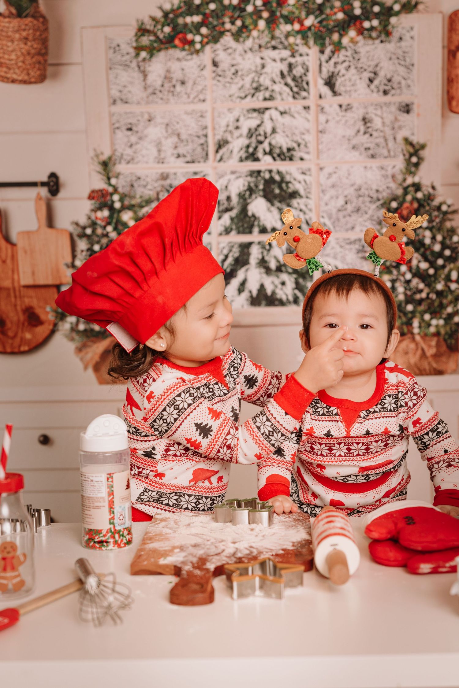 Two people in matching holiday sweaters bake Christmas cookies together at a white counter.
