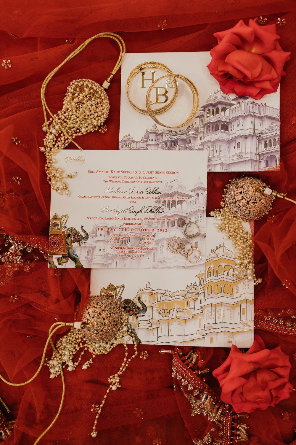 Wedding invitation cards with gold details and architectural sketches laid on red fabric with decorative elements.