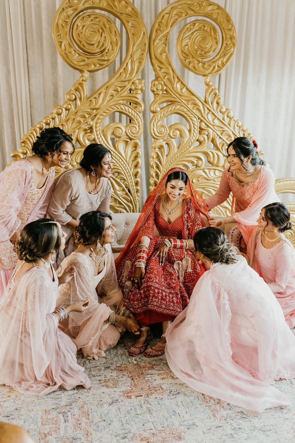 Wedding party in pink and red attire gathered around ornate gold backdrop during celebrations.