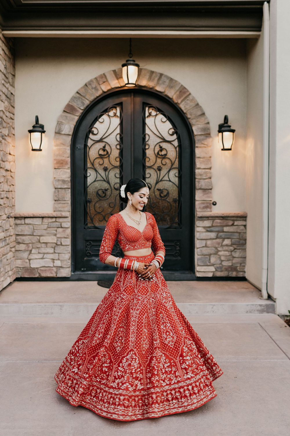 A stunning red and gold embroidered bridal lehenga captured in elegant poses against a stone architecture backdrop.