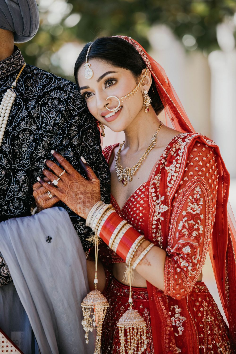 A close-up portrait shot of a couple in traditional Indian wedding attire with gold jewelry and red bridal lehenga.