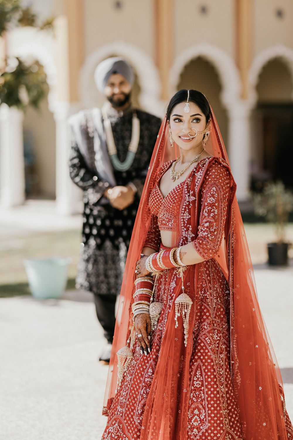 A bride in a red lehenga poses for portraits with intricate jewelry and traditional bridal accessories.