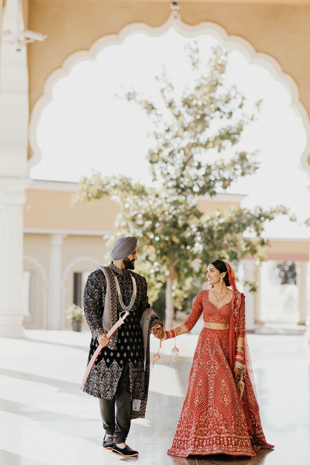 A couple in traditional Indian wedding attire shares romantic moments under white temple arches.