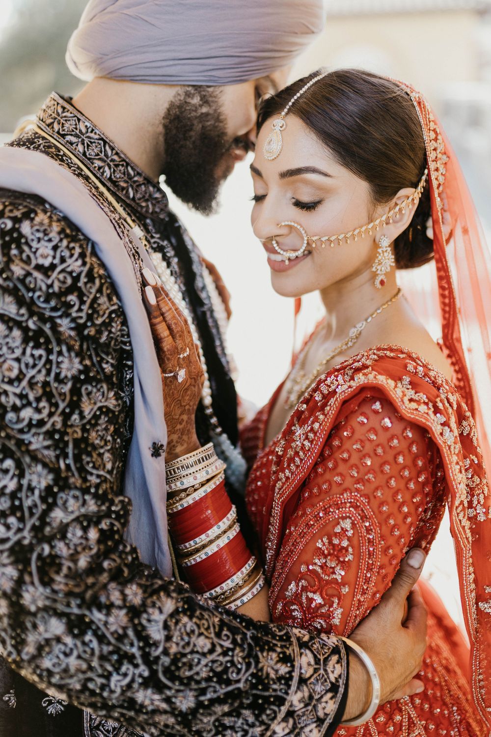 Romantic traditional Indian wedding couple poses in ornate red and black formal attire.