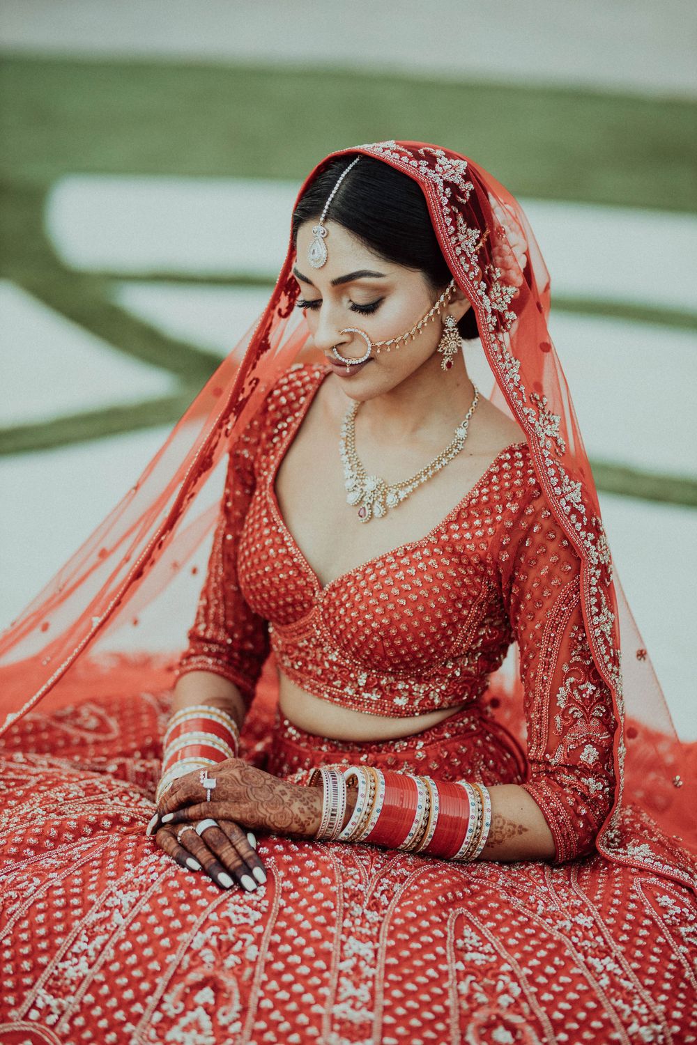 Traditional Indian bridal attire featuring detailed embroidery work and jewelry against a garden background.