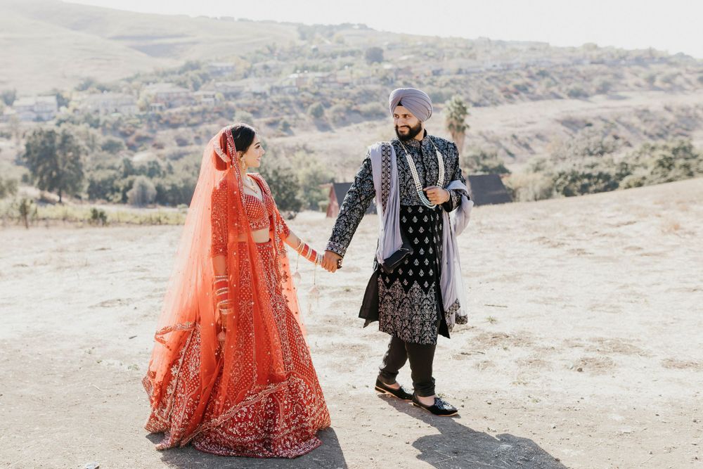Wedding couple in traditional Indian clothing stand together against a desert landscape background.