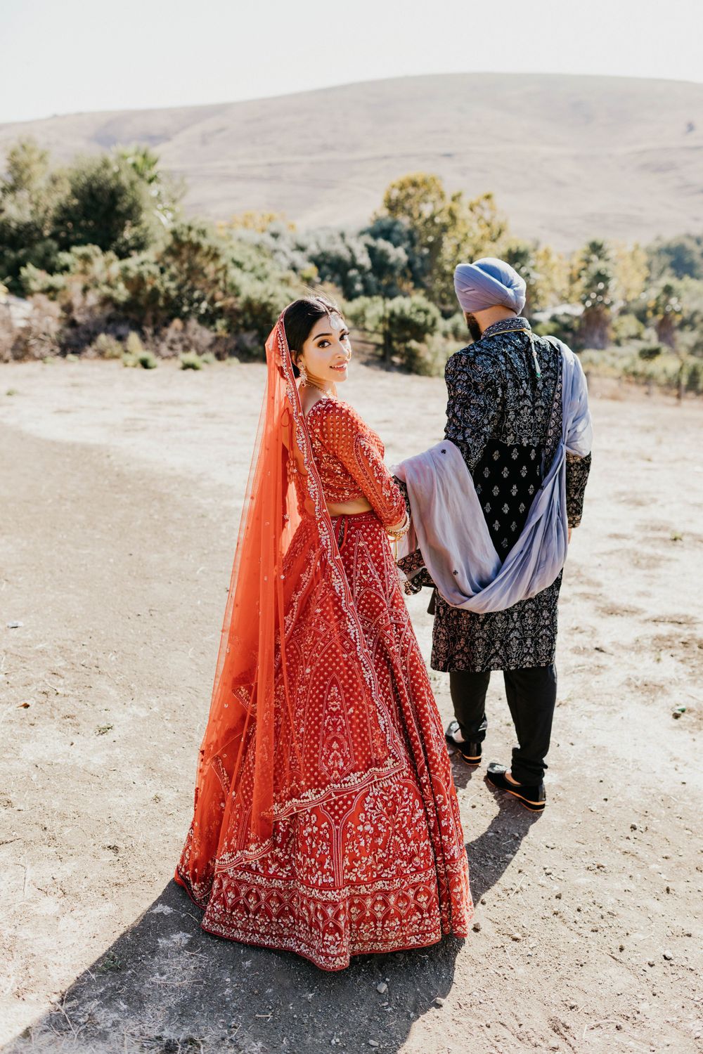 Traditional Indian wedding couple photographed in desert setting with bride in red lehenga.