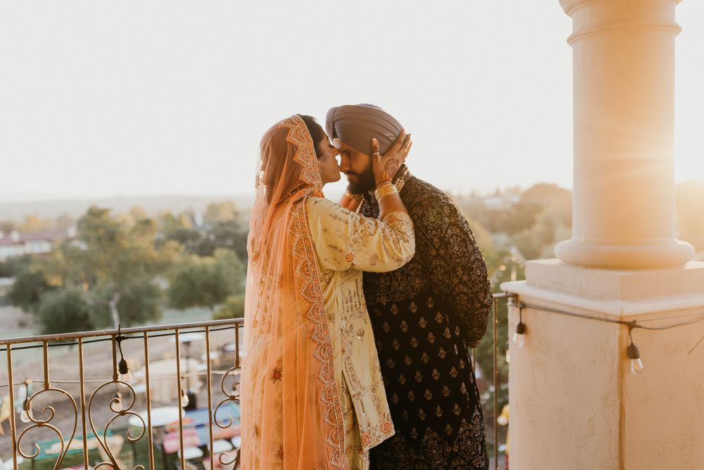 Couple sharing romantic moments on a balcony during sunset at an elegant venue.