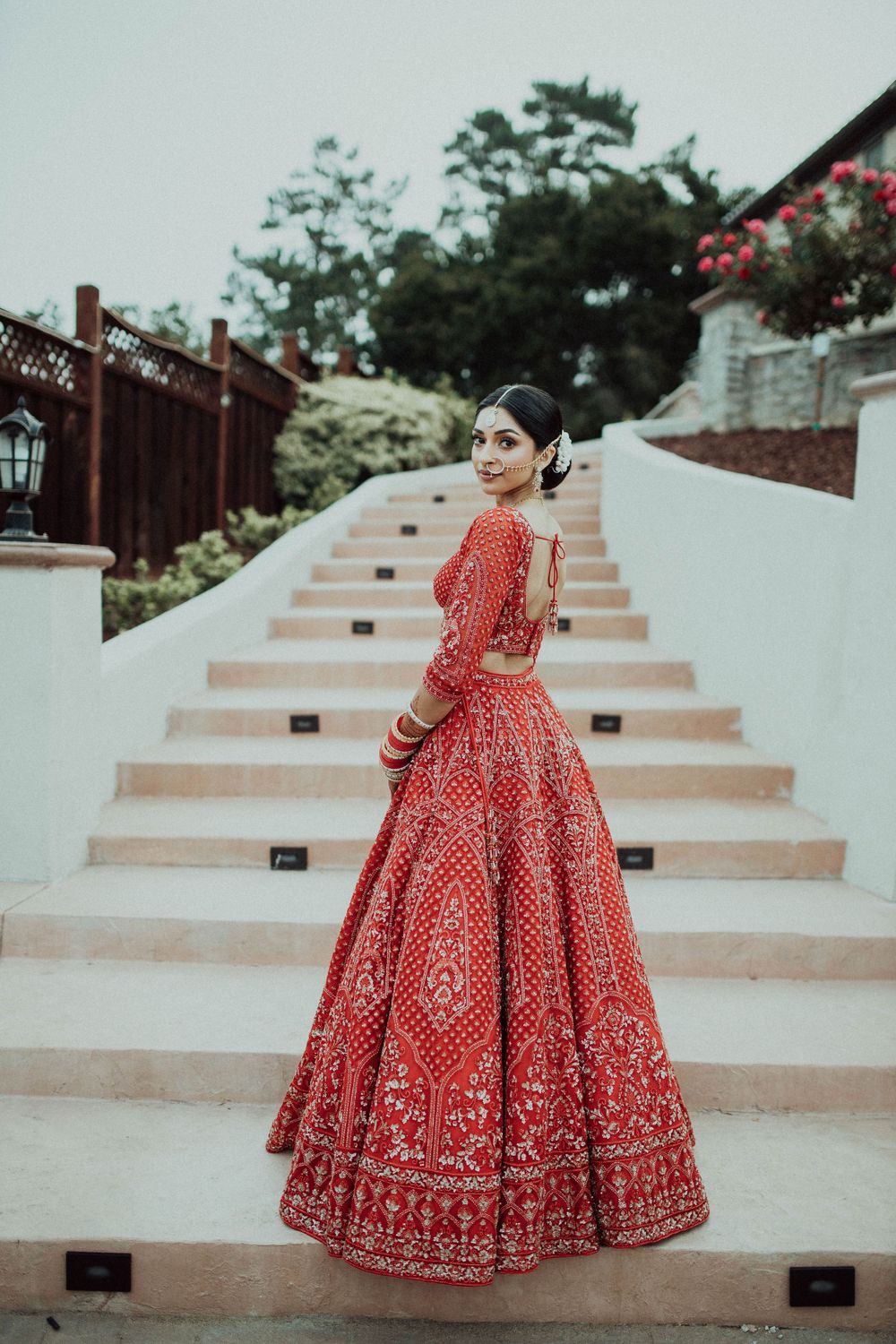 Red bridal lehenga photographed on stone steps showcasing its intricate embroidery and full skirt design.