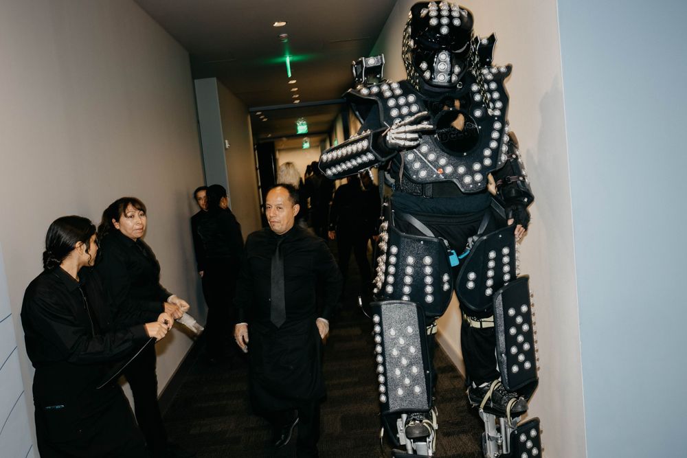 Person in a light-up LED robot costume posing with onlookers in a dark hallway.