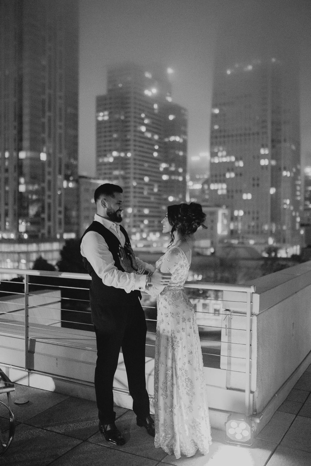 Black and white photo of a couple on a rooftop terrace with city lights in background.