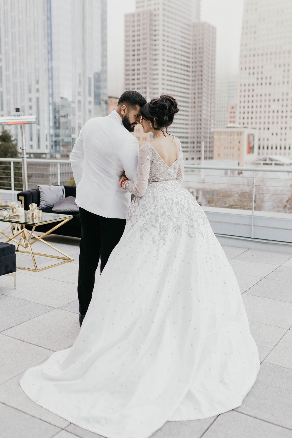 Couple in wedding attire embracing on urban rooftop with skyline view.