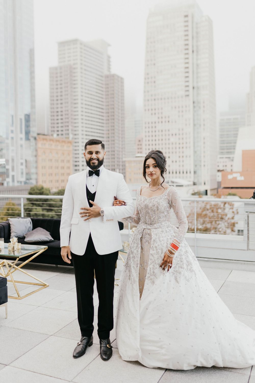 Newlyweds posing for wedding portraits on a rooftop with urban skyline views.