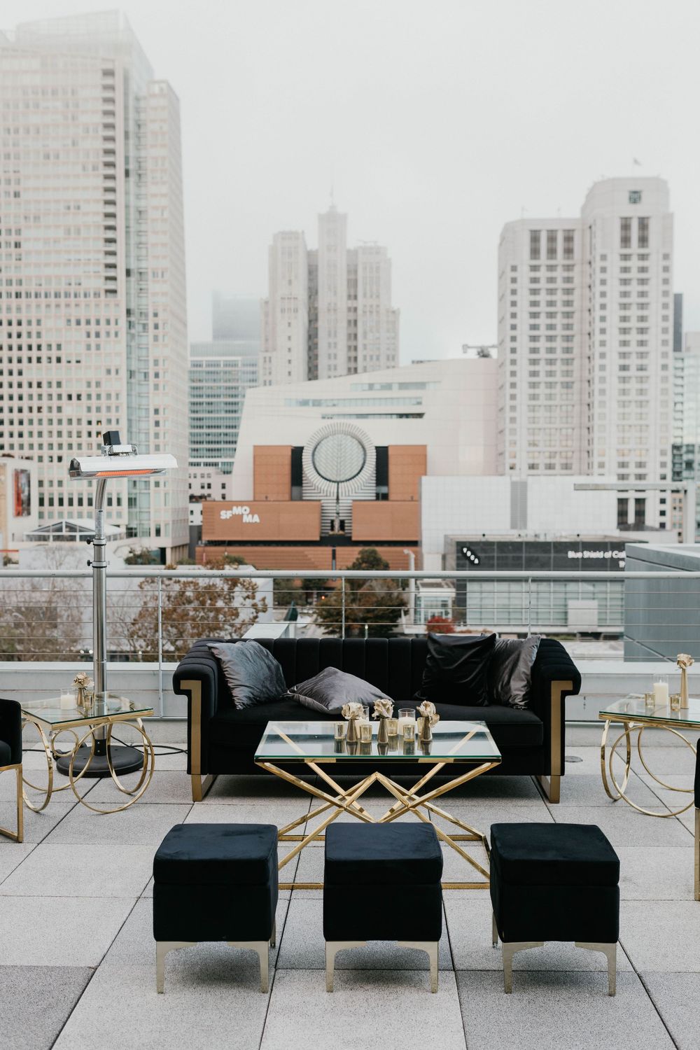Modern black and gold lounge furniture arranged on a rooftop venue with city views.