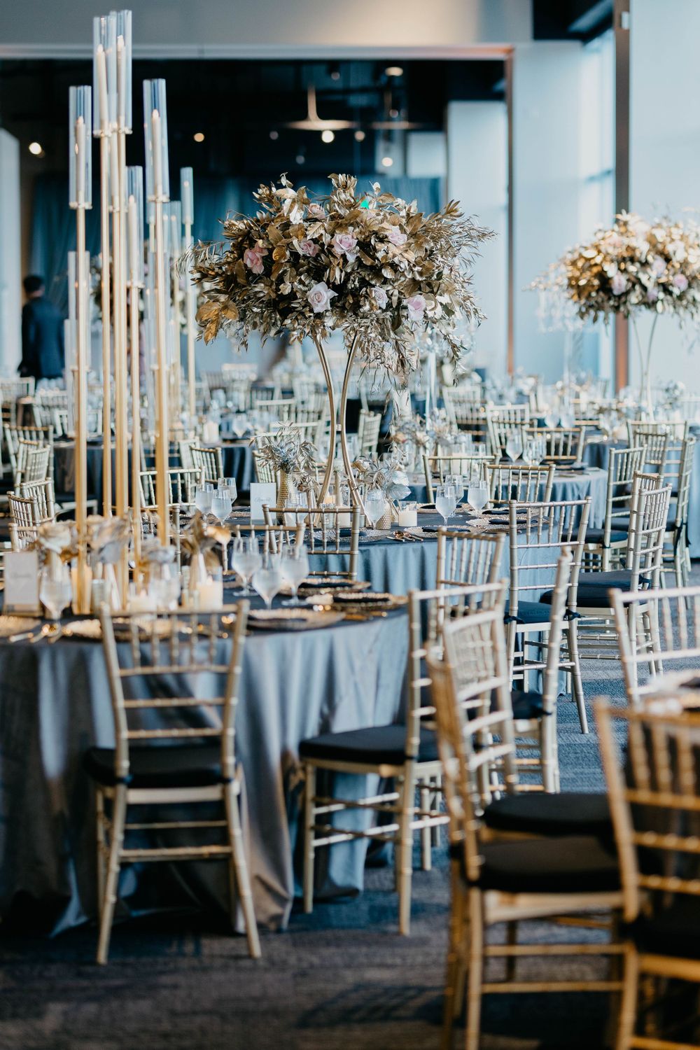 Modern wedding reception venue with tall centerpieces and silver chiavari chairs.
