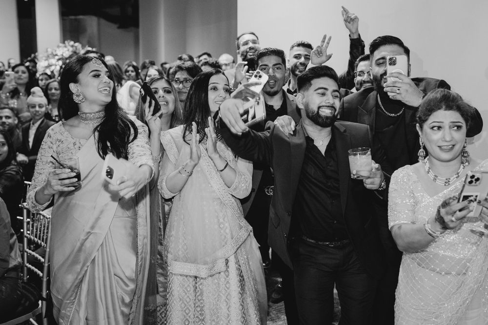 Black and white photo of joyful wedding guests cheering and celebrating at a reception.