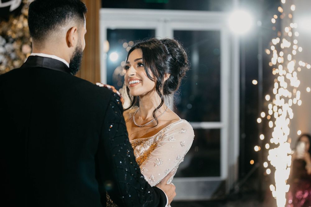 A couple shares an intimate moment in front of decorative string lights at an evening event.