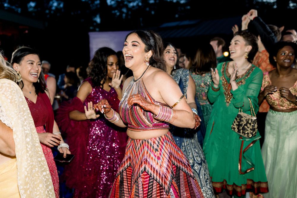 Wedding reception guests dancing together in colorful dresses at an indoor celebration.