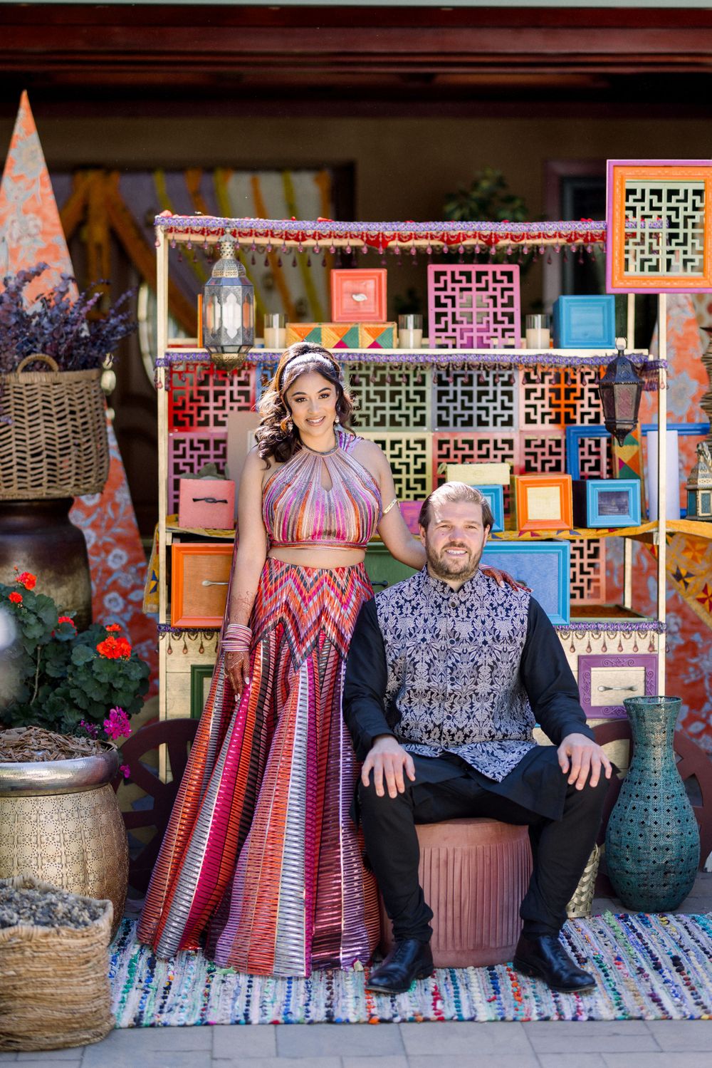 A couple poses in coordinated outfits among decorative market stalls with colorful displays.