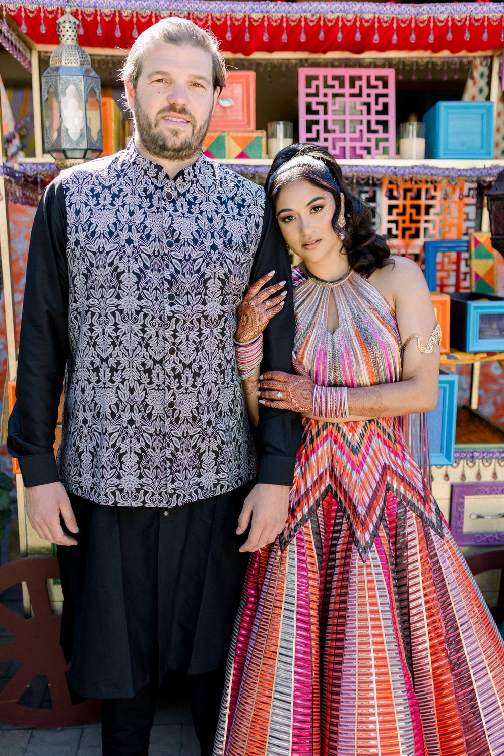 A couple in matching patterned outfits pose together against a colorful market backdrop.