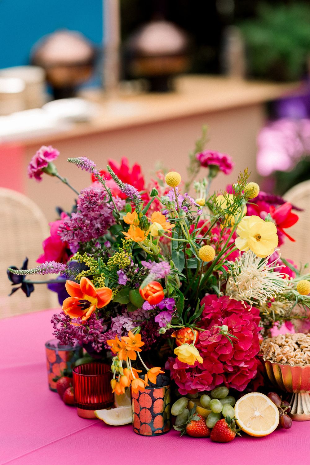 Colorful floral centerpieces with citrus accents arranged on pink tablecloths.