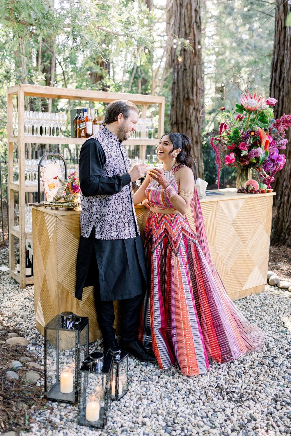 Romantic outdoor bar setup with couple enjoying drinks among forest trees and decorative elements.