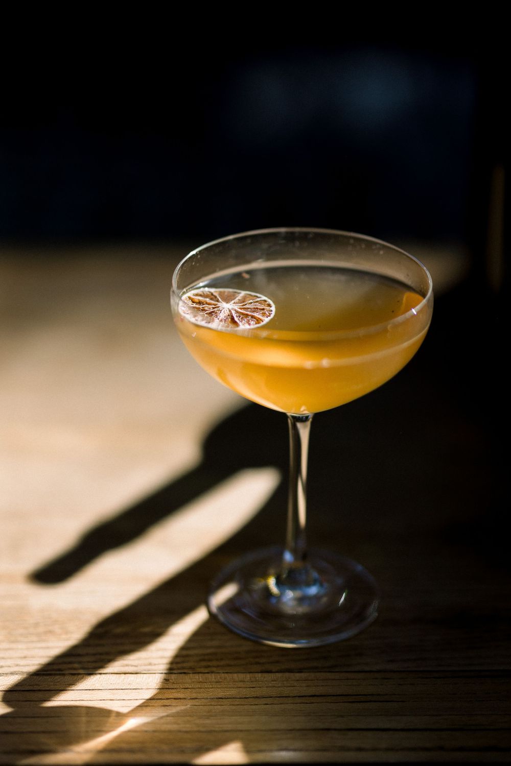 Elegant cocktail in coupe glass with citrus garnish captured in dramatic lighting.