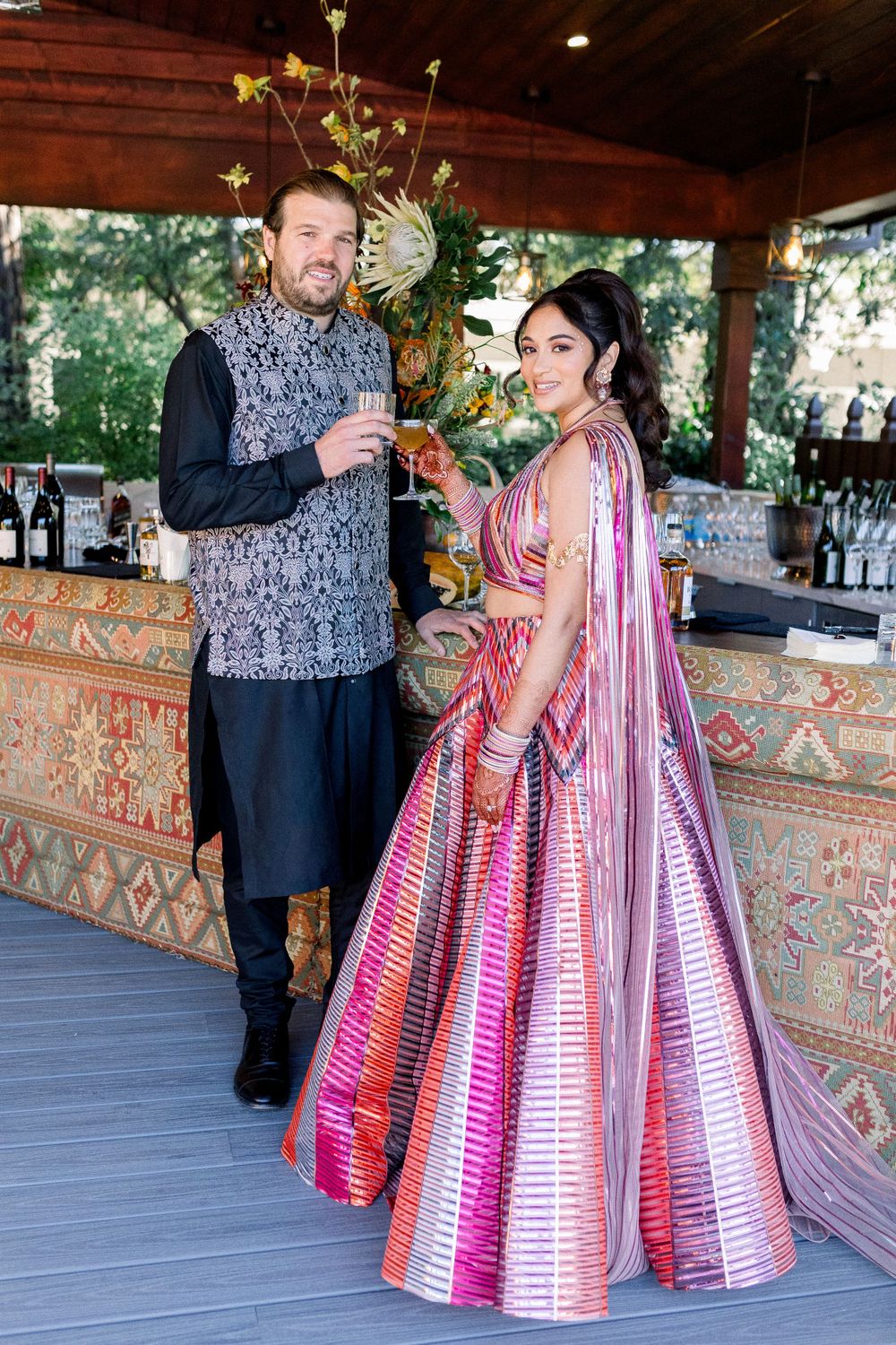 A couple poses together in formal attire, featuring a pink and white striped ballgown dress at an outdoor event.